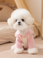 White dog sitting in a pink and yellow striped jumpsuit with a ruffled collar.