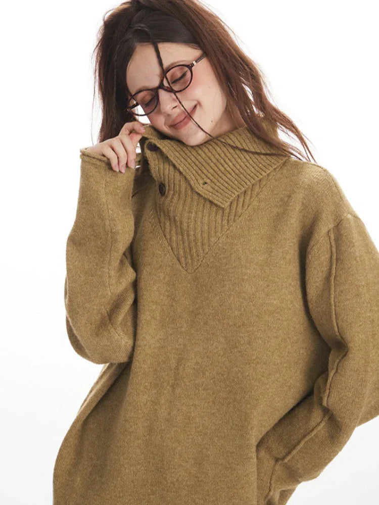 Close-up of a model wearing a tan oversized knit sweater with a wide collar and button detail, touching her collar and smiling.