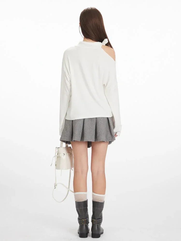 Full-body back view of a woman wearing a white long-sleeved top with one shoulder exposed and a grey pleated skirt.