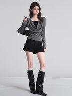 Full-body shot of a model wearing a grey long-sleeved top, black shorts, and black boots.