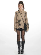Front view of a model wearing a distressed knit cardigan with a graphic print, paired with black shorts, star-patterned tights, and black boots.