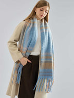 Woman wearing a beige coat and a blue and tan plaid scarf, with one hand in her pocket.