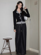 Woman standing in a fitting room wearing a black and grey layered top with ruffled trim and dark wide-leg jeans, holding a silver handbag.