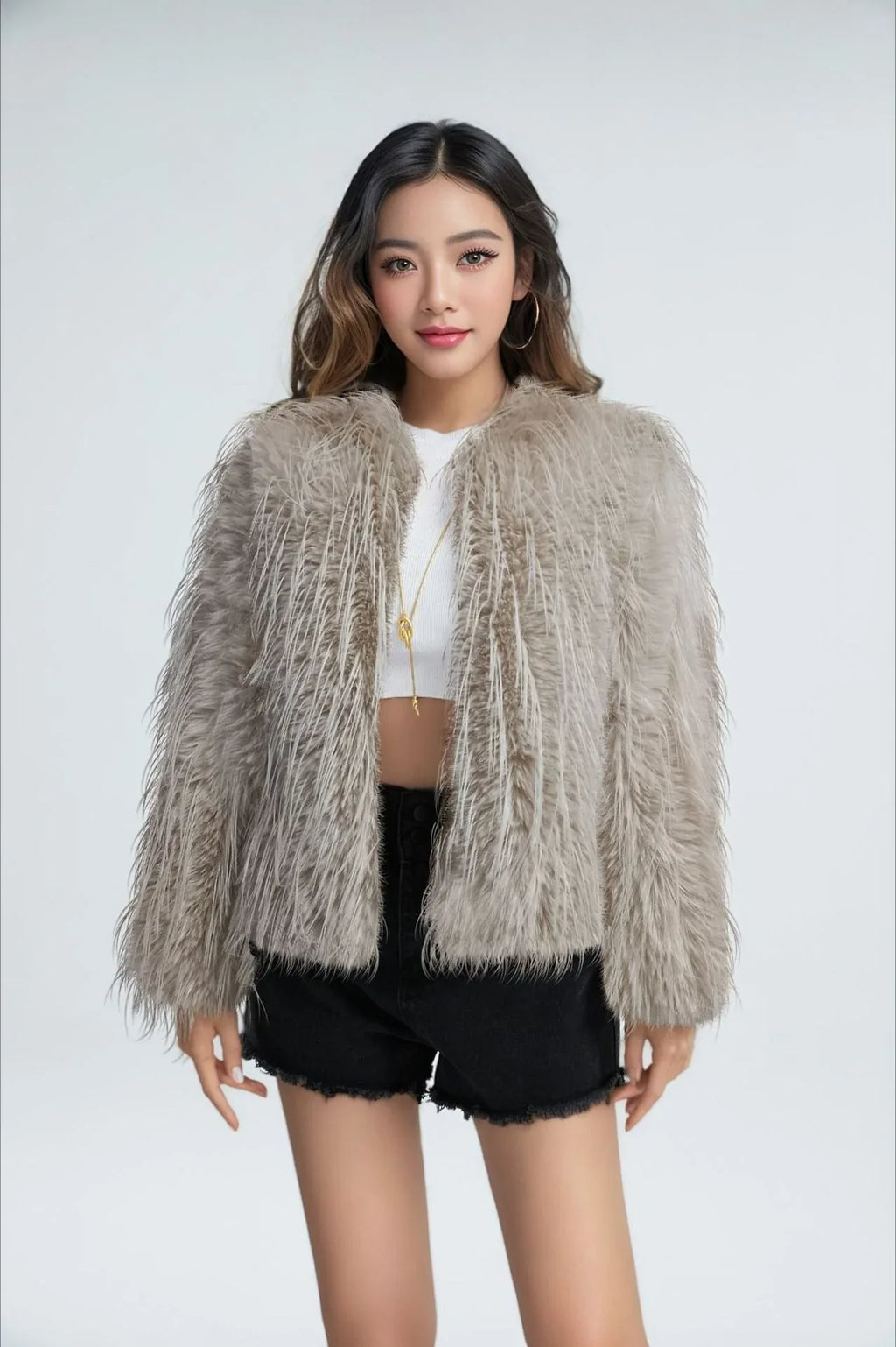Model wearing a grey faux fur jacket with a fringed texture, a cropped length, and an open front, paired with a white crop top and black shorts.