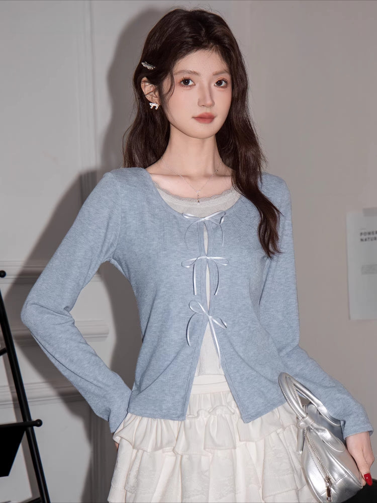 Woman wearing a light blue knit cardigan with white ribbon ties and a white layered skirt.