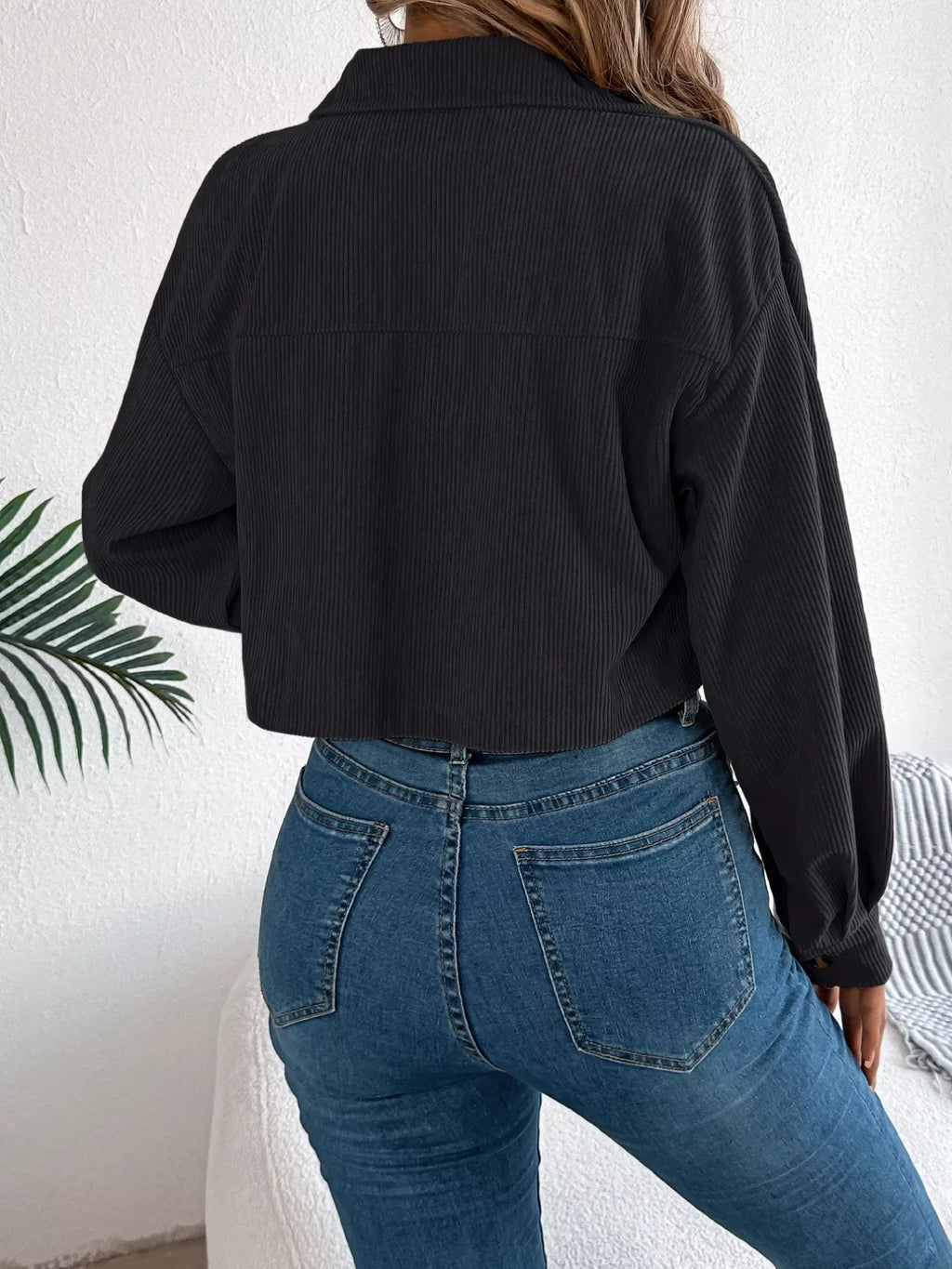 Back view of a woman wearing a black corduroy cropped jacket and blue jeans.