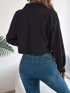 Back view of a woman wearing a black corduroy cropped jacket and blue jeans.