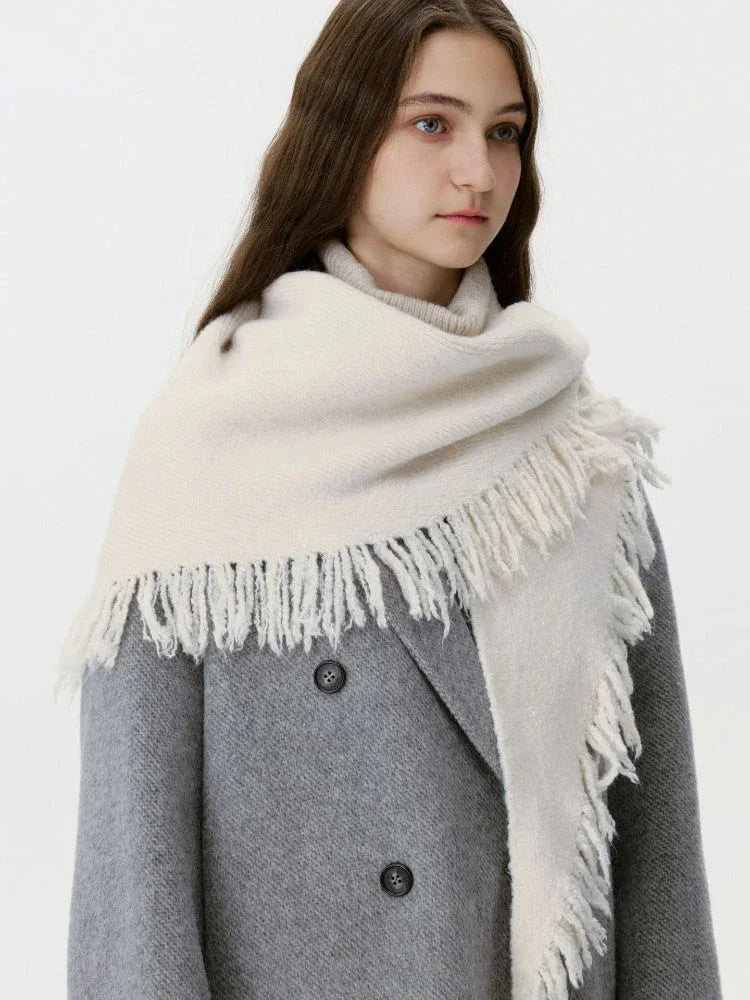 Model wearing a cream-colored oversized scarf with fringe detail over a grey coat
