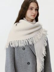 Model wearing a cream-colored oversized scarf with fringe detail over a grey coat