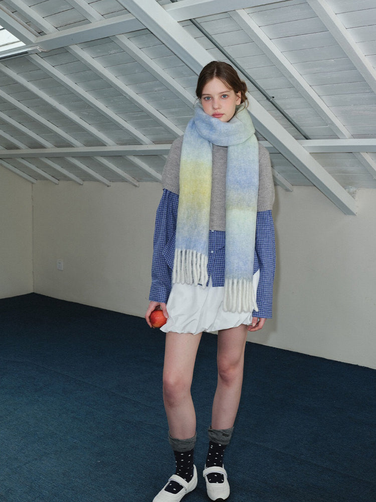 Full body shot of a woman wearing an oversized ombre scarf, grey sweater, blue plaid shirt, and white shorts.