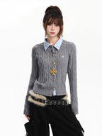 Woman wearing a grey cable knit cardigan with a light blue collared shirt underneath, gold cross necklace, and black cargo pants.