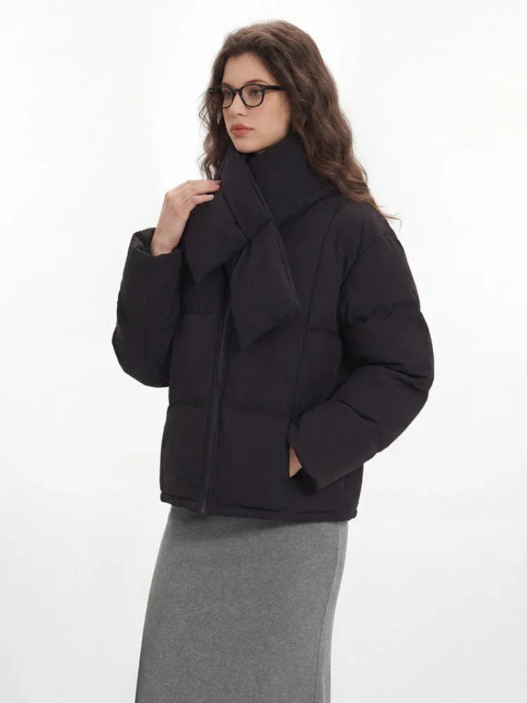 Woman adjusting the scarf on her black puffer jacket, with the grey skirt and tote bag visible.