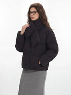 Woman adjusting the scarf on her black puffer jacket, with the grey skirt and tote bag visible.