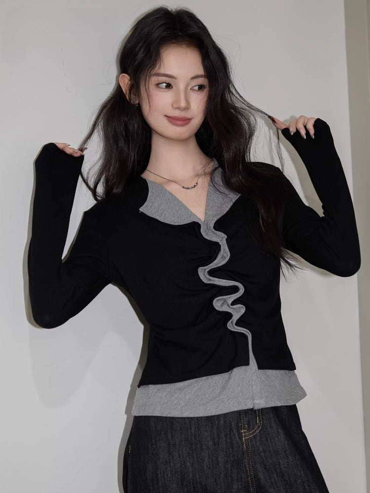 Woman in a black and grey layered top with ruffled trim, smiling and playing with her hair.