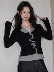 Woman in a black and grey layered top with ruffled trim, smiling and playing with her hair.