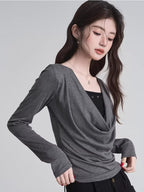 Close-up of a woman wearing a grey draped long-sleeve top over a black camisole.