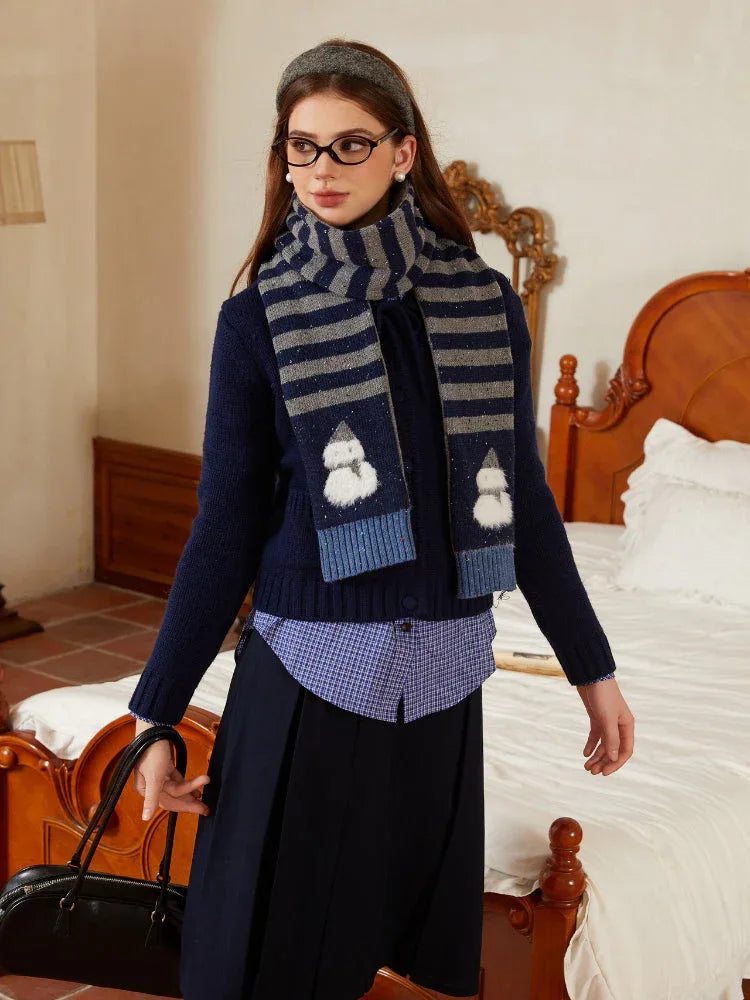 Woman sitting on the edge of a bed, holding a black handbag, wearing a winter-themed outfit with a scarf and boots.