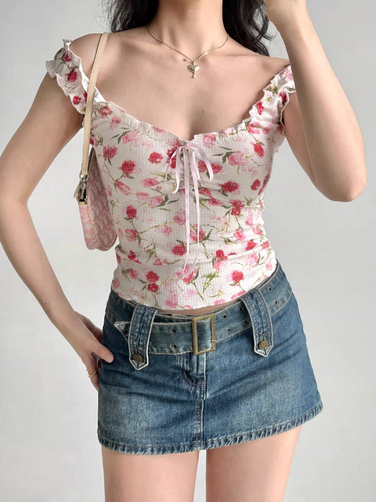Full body shot of a woman wearing a white floral print top, blue denim mini skirt, and a pink handbag.