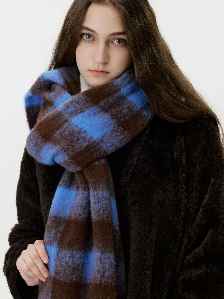Close-up of a woman wearing a blue and brown plaid scarf with fringe, the texture of the fuzzy knit is visible.