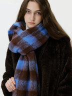 Close-up of a woman wearing a blue and brown plaid scarf with fringe, the texture of the fuzzy knit is visible.