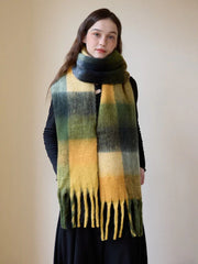 Woman wearing a long, oversized scarf with a green, yellow, and black plaid pattern and fringe detail.