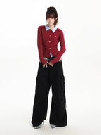 Full body shot of a woman in a red cable knit cardigan, light blue collared shirt, black cargo pants, and a furry belt.