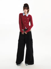 Full body shot of a woman in a red cable knit cardigan, light blue collared shirt, black cargo pants, and a furry belt.