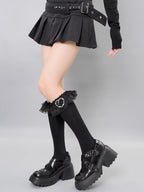 Full body shot of a model in a black pleated mini skirt, black knee-high socks with lace trim, and black buckled platform shoes.