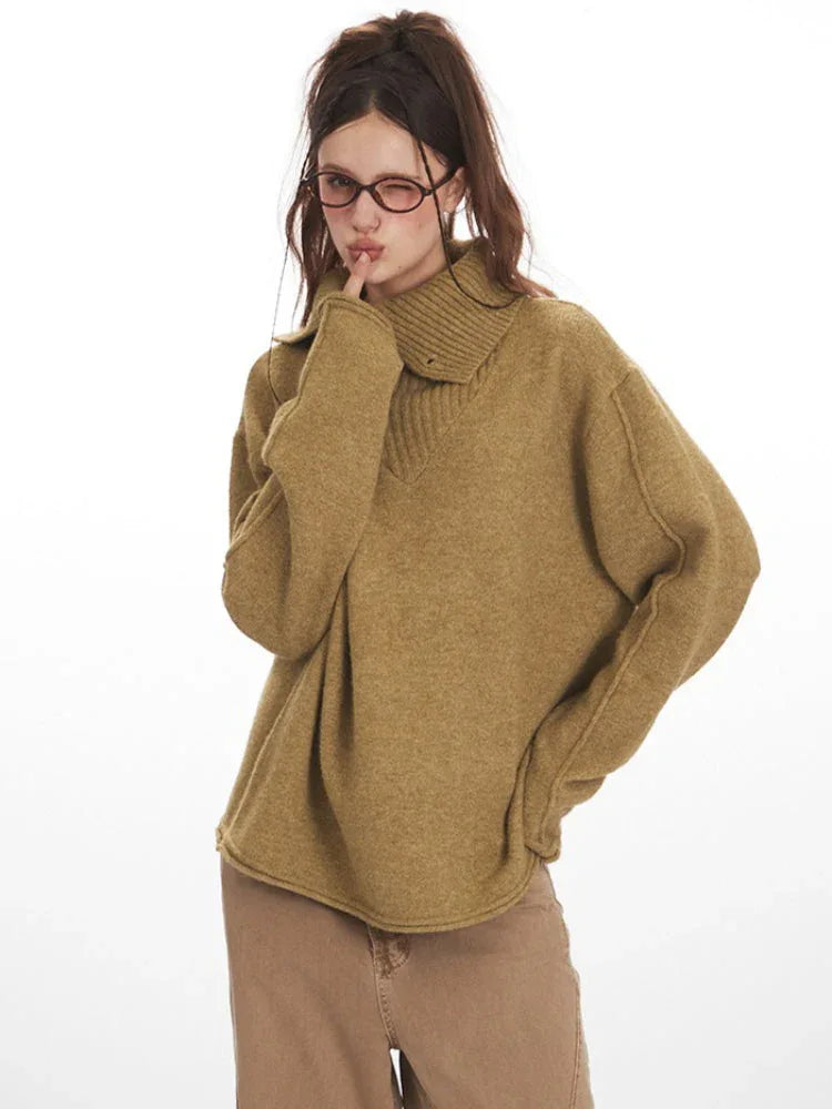 Close-up of a model wearing a tan oversized knit sweater with a wide collar and button detail, looking over her shoulder and winking.