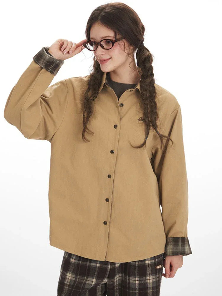 Close-up of a model wearing a tan button-down shirt with plaid cuffs, adjusting her glasses.