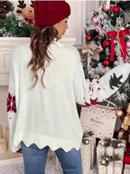 Back view of a woman wearing a white knitted sweater with a Christmas tree and snowflake print, standing in front of a Christmas tree.