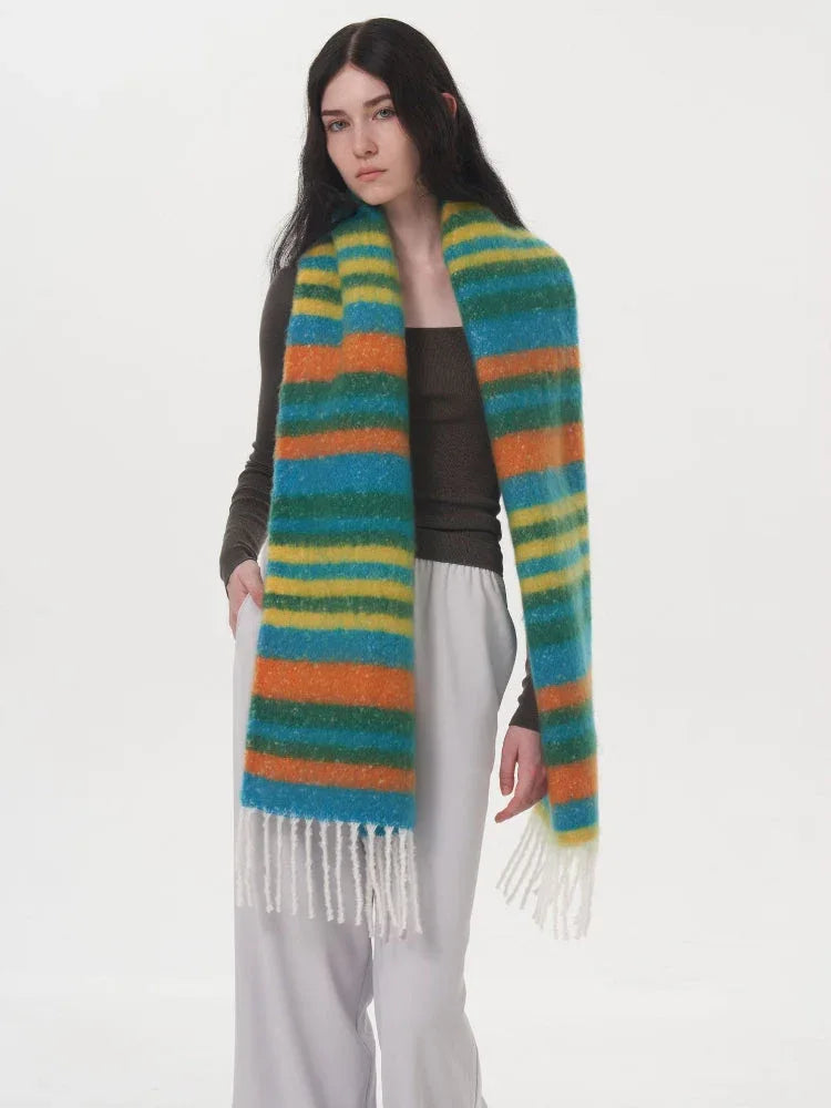 Full body shot of a woman wearing a long-sleeved dark top and light grey pants, showcasing a long, colorful striped scarf.