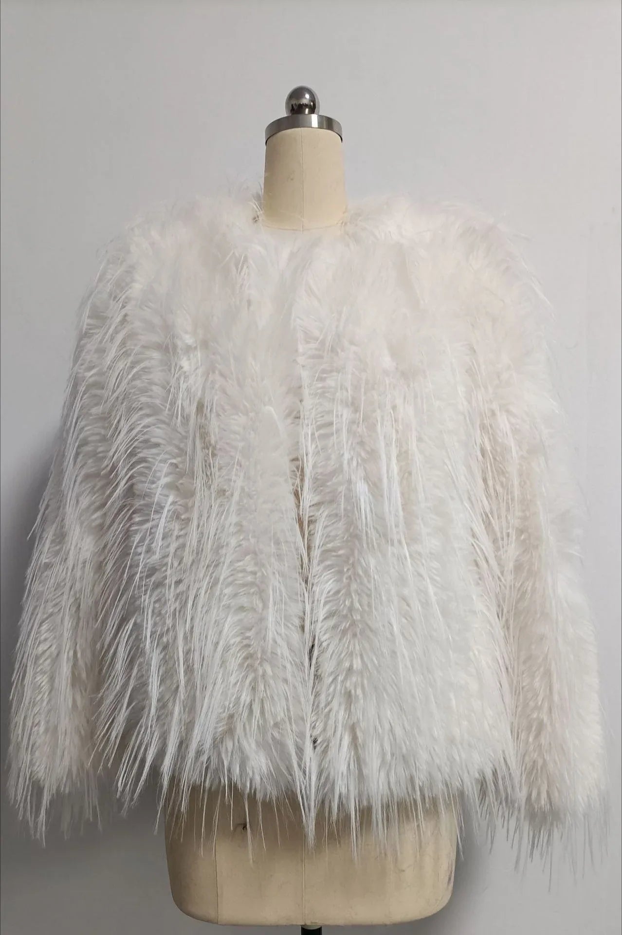 White faux fur jacket with a shaggy, fringed texture displayed on a mannequin.