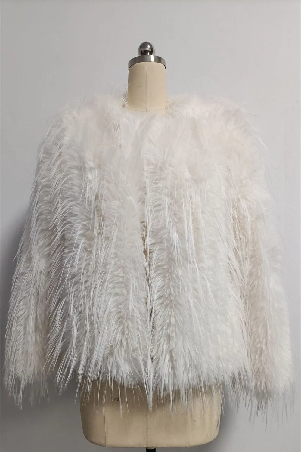 White faux fur jacket with a shaggy, fringed texture displayed on a mannequin.