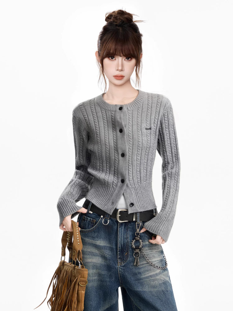 Woman wearing a grey cable knit cropped cardigan with blue jeans and a brown fringed bag