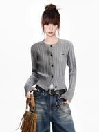 Woman wearing a grey cable knit cropped cardigan with blue jeans and a brown fringed bag