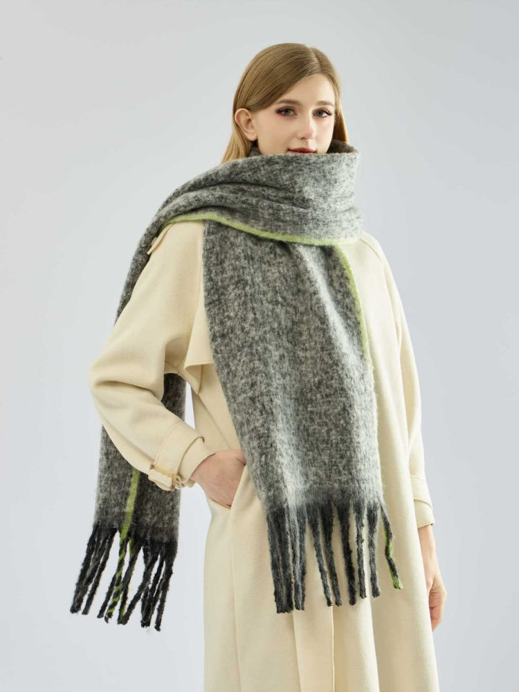 Close-up of a woman wearing a long, grey, textured knit scarf with fringe detail and lime green trim.