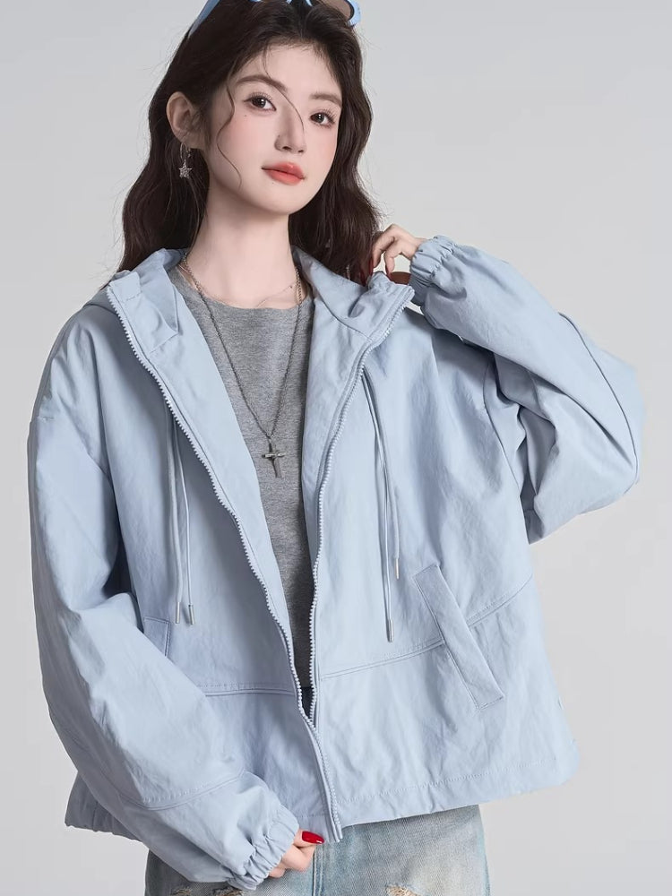 Woman wearing a light blue hooded jacket with a grey t-shirt and silver necklace, close-up on upper body.