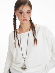 Close-up of a model's face wearing a white off-the-shoulder long-sleeve top and a necklace with a heart pendant.