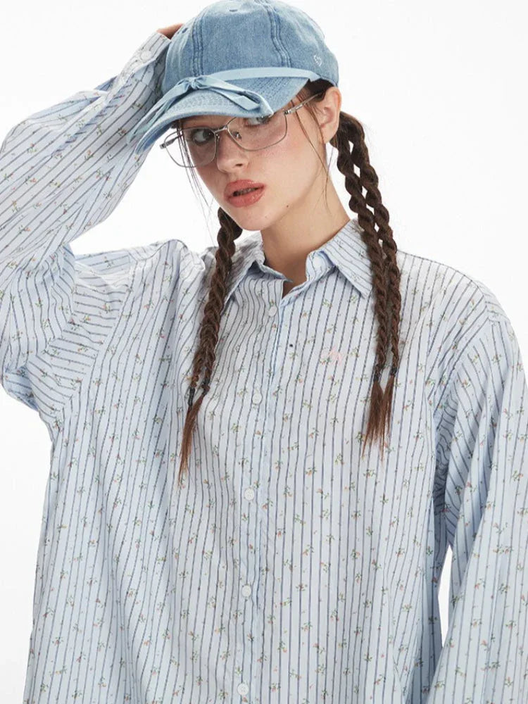 Close-up front view of the woman's face and the detail of the light blue pinstripe shirt with floral accents.