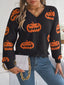 Woman wearing a black long-sleeve v-neck cropped knit sweater with an all-over orange pumpkin print and a distressed hem, paired with blue jeans and a white quilted handbag with a gold chain strap.