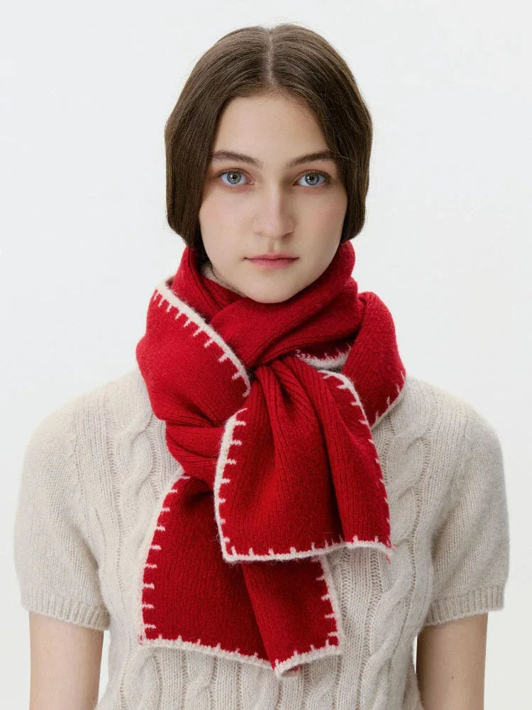 Woman wearing a red knit scarf with white contrast stitching over a cream cable knit sweater, front view.