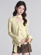 Close-up of a woman wearing a light yellow textured knit top with a draped neckline and ruffle detail.