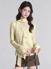 Close-up of a woman wearing a light yellow textured knit top with a draped neckline and ruffle detail.