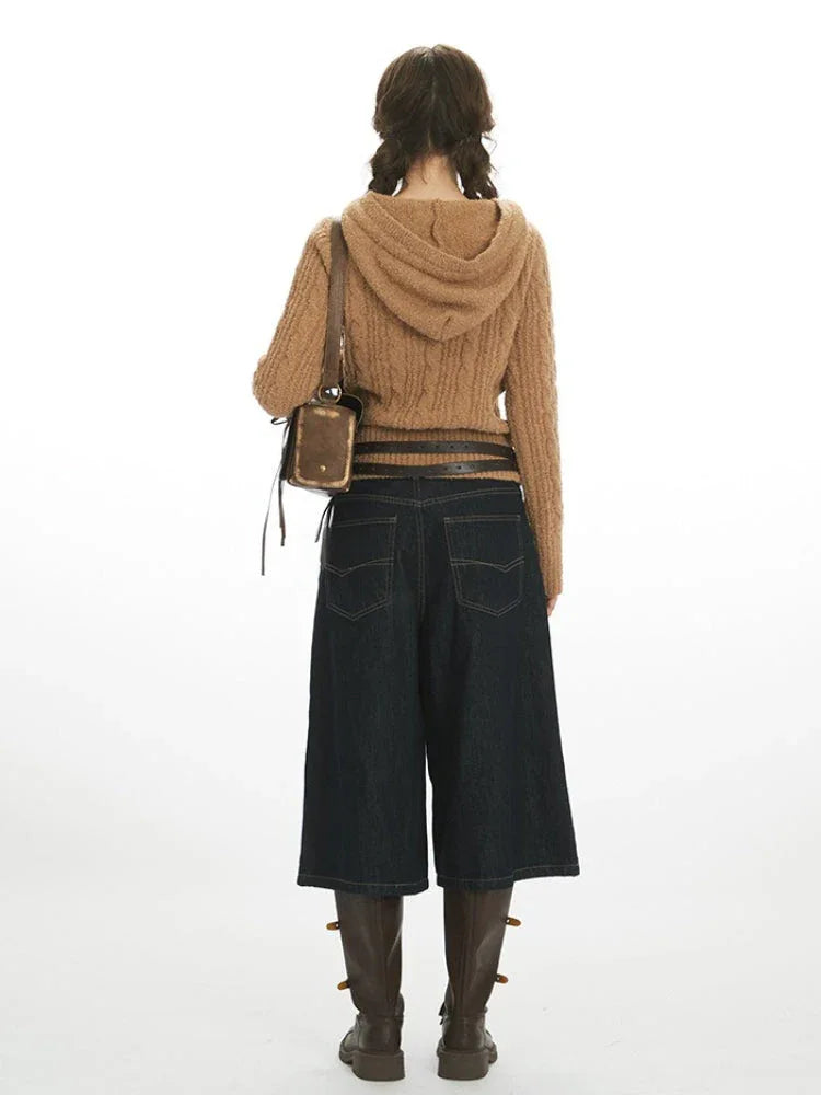 Back view of a woman wearing a brown cable knit hooded sweater with buttons and pom-poms, dark wash wide-leg cropped jeans, a black belt, and brown boots. Secondary image