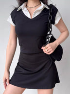 Full body shot of a model wearing a black v-neck top layered over a white collared shirt, paired with a black skirt and handbag.