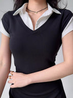 Detailed view of the neckline and collar of a black v-neck top layered over a white collared shirt, with gold rings on the model's fingers.
