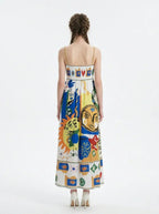 Back view of a woman wearing a white maxi dress with a colorful abstract print and spaghetti straps, standing against a white background.