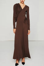 A woman models a long, brown, long-sleeved dress with asymmetrical draping on the left shoulder and ruching on the right side of the bodice.