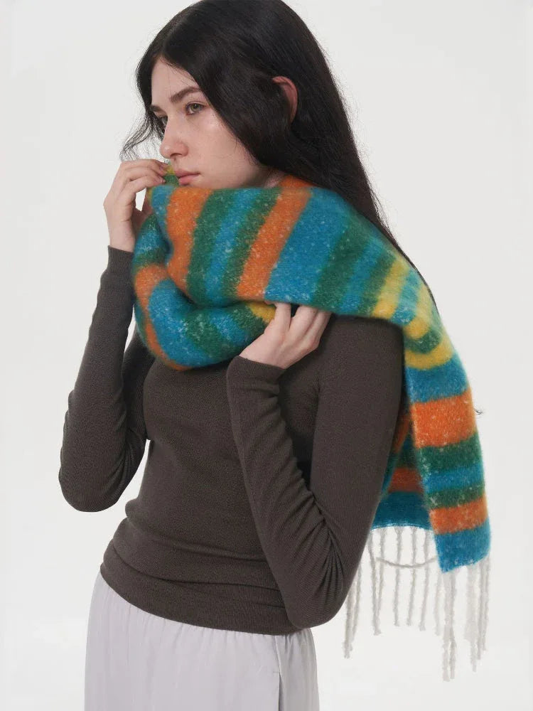 Close-up of a woman wearing a long-sleeved dark top and light grey pants, adjusting a colorful striped scarf around her neck.